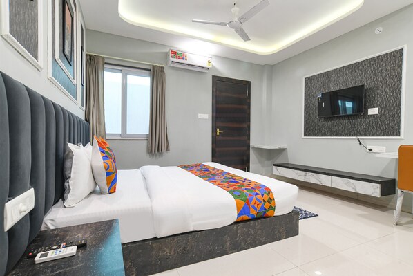 A modern hotel room with a bed, a desk, a TV, and a ceiling fan. - Fabhotel Rk (Indore)