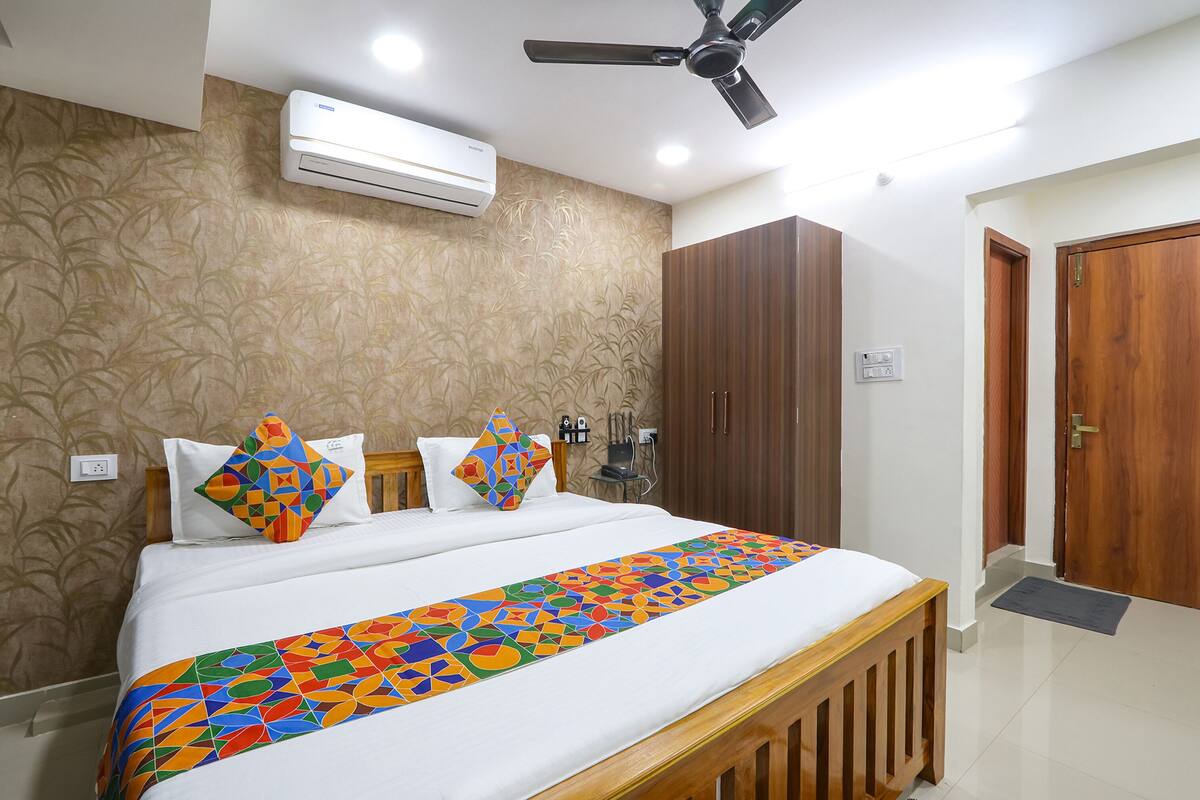 Un letto ben rifatto con una coperta colorata a motivi geometrici, una ventola a soffitto e un armadio in una camera d'albergo.