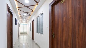 A hallway with wooden doors, a tiled floor, and a ceiling with recessed lighting. - Fabhotel Vgr Comforts (Hyderabad)