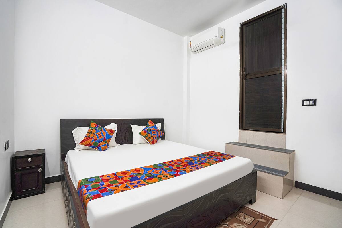 A neatly arranged bedroom with a bed, pillows, a bedside table, and a window with a curtain.