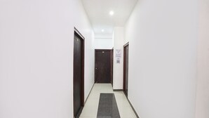 A narrow hallway with white walls and dark wooden doors, leading to a room with a sign indicating a 4-star rating. - Fabhotel Om Palace (Faizabad)