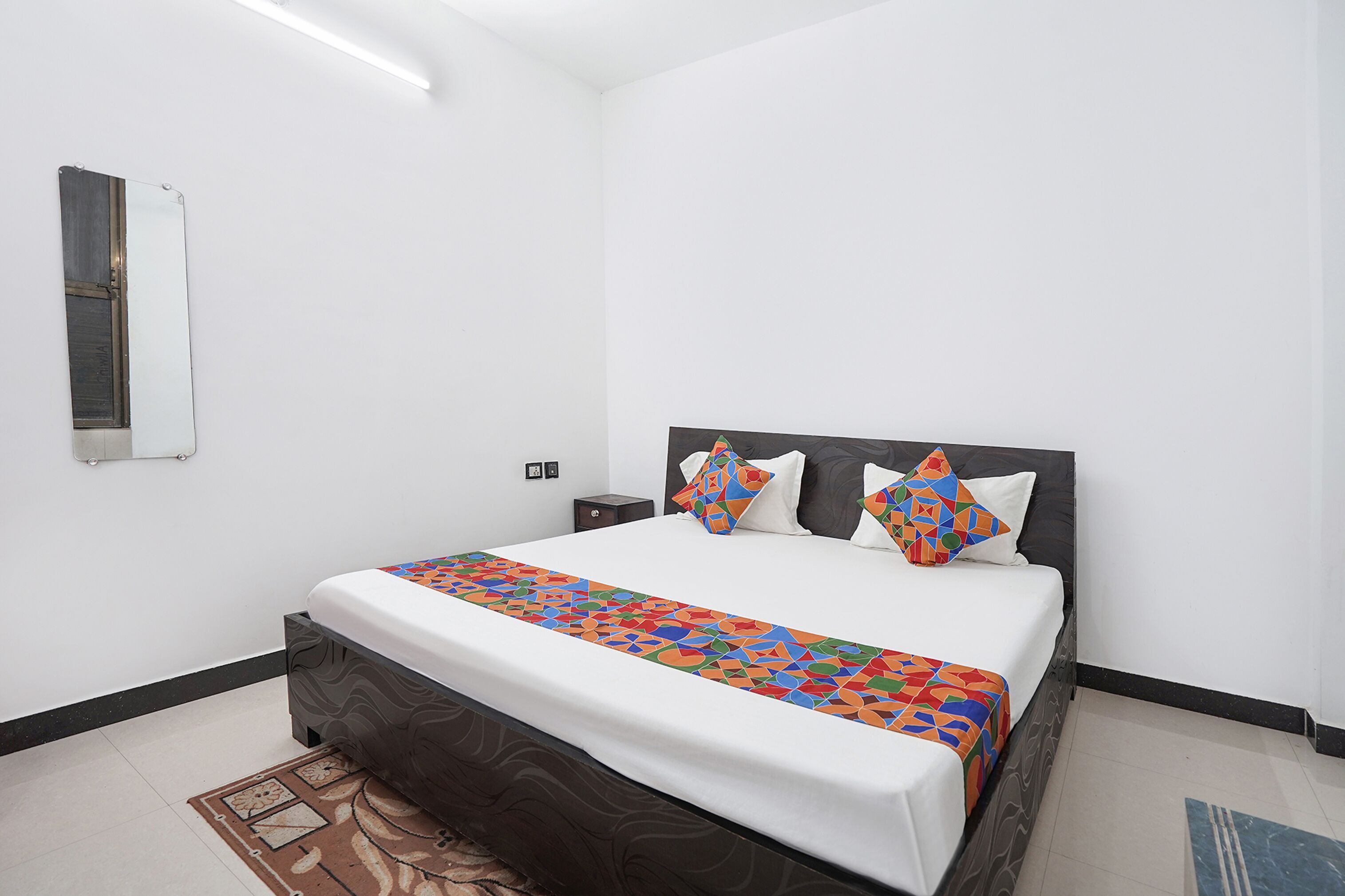 A neatly made bed with a colorful geometric-patterned bedspread, a dark headboard, and two bedside tables with lamps.