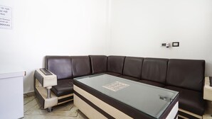 A corner room with a brown leather sofa, a glass-top coffee table, a small white cabinet, and a tiled floor. - Fabhotel Om Palace (Faizabad)