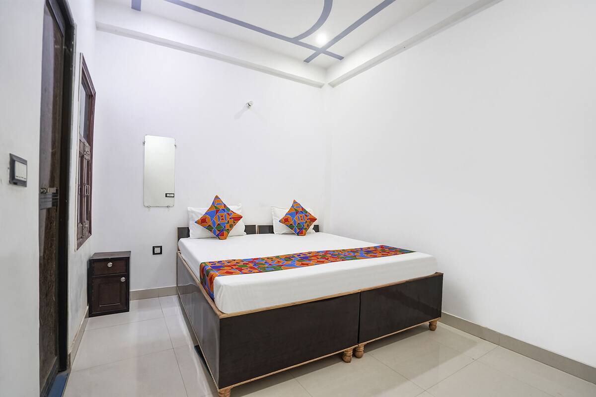 A bedroom with a bed, a nightstand, a wall-mounted light, and a door.