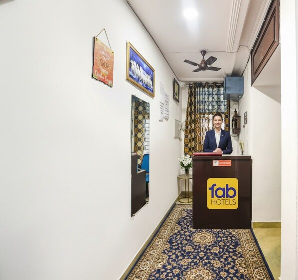 A hotel reception area with a receptionist, a sign reading "fab HOTELS", and a patterned carpet. - Fabhotel Silver Stone (Noida)