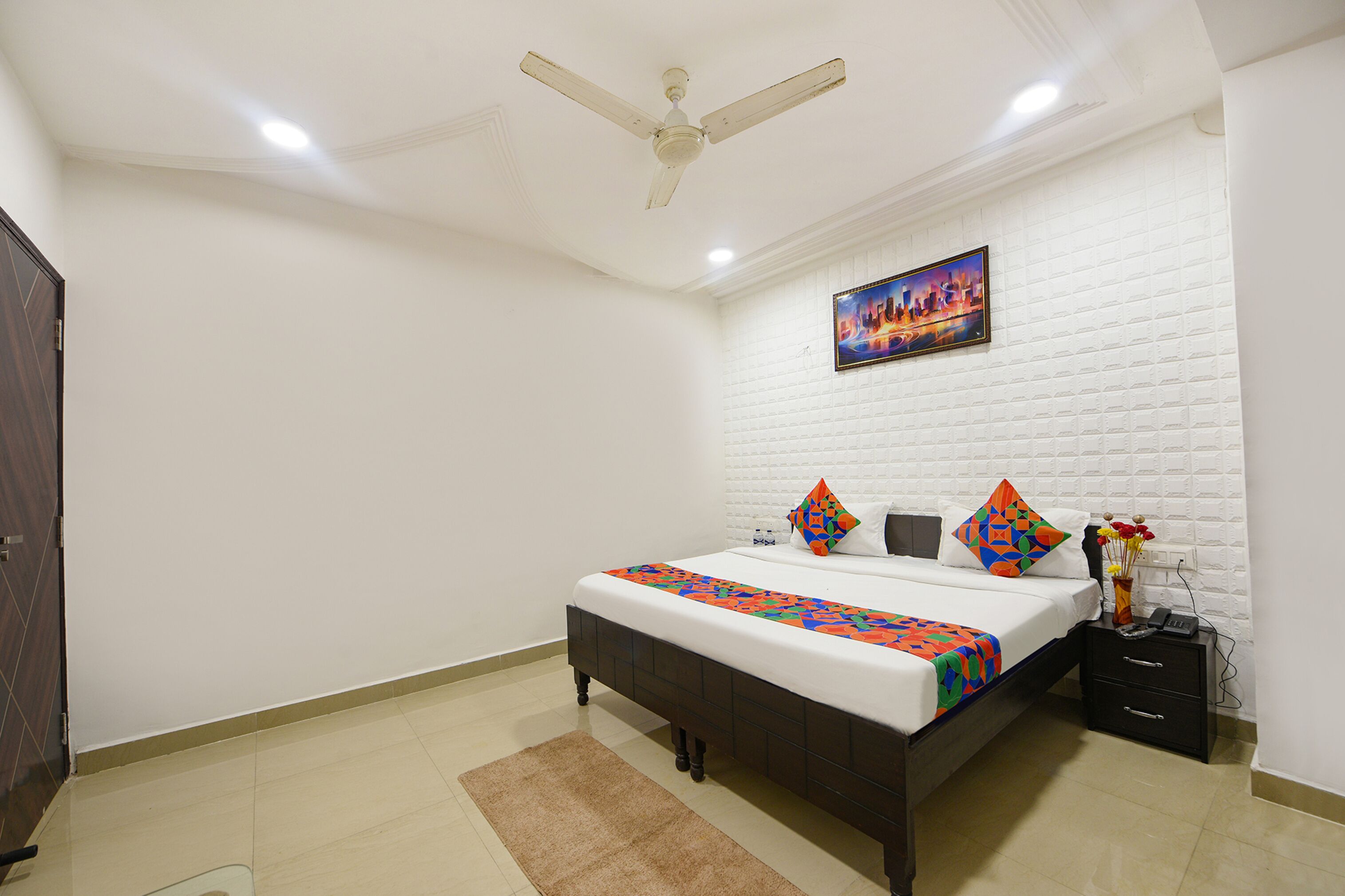 A bedroom with a bed, a nightstand, a ceiling fan, a painting on the wall, and a door.