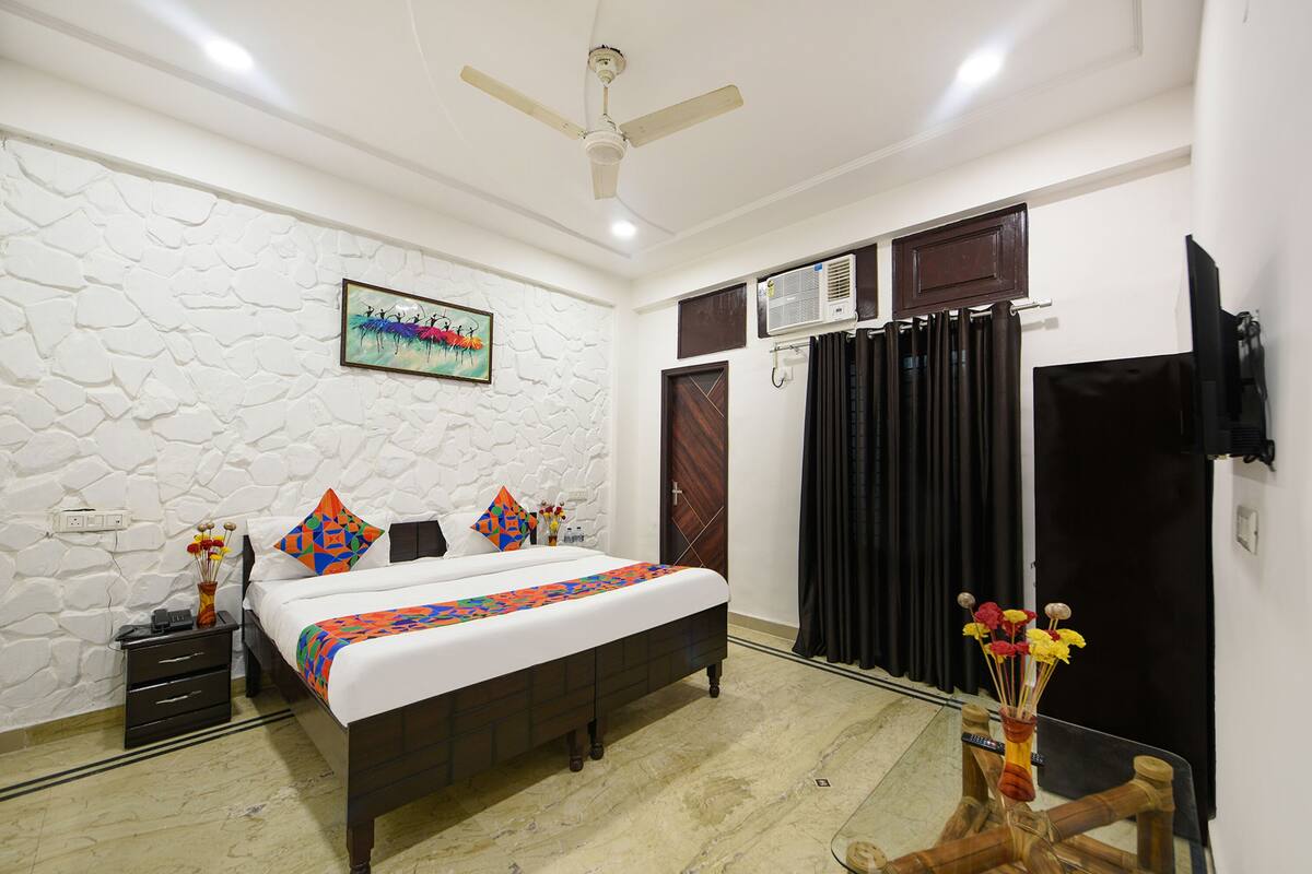 A bedroom with a bed, a ceiling fan, a wall-mounted air conditioner, and a television on the wall.