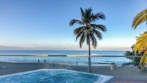 Zona de piscina con vista al océano y palmeras.
