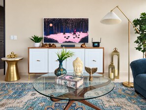 Ein modernes Wohnzimmer mit einem Glastisch, einer Couch, einem Fernseher und Dekorationen auf einer weißen Kommode.