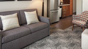 A living room with a grey sofa, patterned cushions, a patterned rug, a kitchen area with a refrigerator, microwave, and wooden cabinets. - Coachella Fun and Luxury in the Desert - Marriott Shadow Ridge II - The Enclaves (Palm Desert)