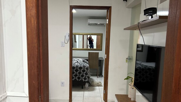 Un couloir menant à une chambre à coucher équipée d’un lit, d’une télévision et d’un miroir.