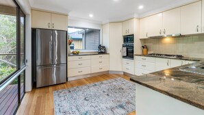 A modern kitchen with stainless steel appliances, white cabinetry, and a large window overlooking greenery.
