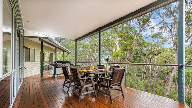 A wooden deck with a table and chairs, overlooking a forested area.