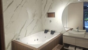 Een moderne badkamer met een vrijstaand bad, een grote spiegel en een houten bankje.