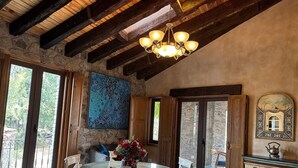 A dining area with a round table, chairs, a chandelier, and a stone wall with a painting. - Departamento Michelangelo Master (Val'Quirico)