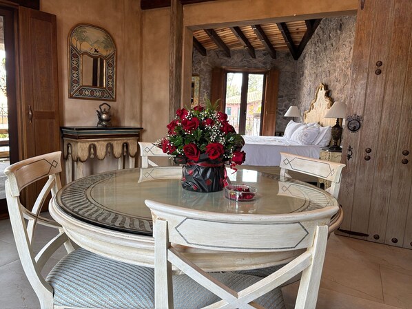 A round table with chairs, a vase of red roses, and a stone wall in the background. - Departamento Michelangelo Master (Val'Quirico)