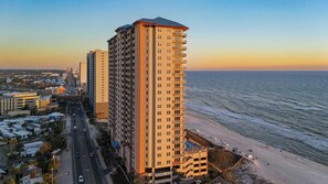 A high-rise hotel with multiple balconies, a beach view, and a parking area adjacent to the building.