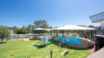 Una piscina con zona techada, tobogán y césped.