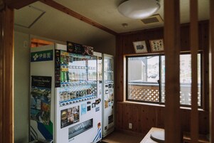 A room with a vending machine stocked with beverages and snacks, a wooden interior, and a window with a view of the outside.