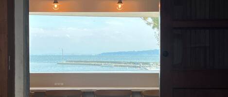 A view from a window with a table and chairs, overlooking a body of water and a distant pier.
