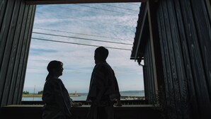 Dos personas de pie junto a una ventana con vistas al cielo y una estructura distante.