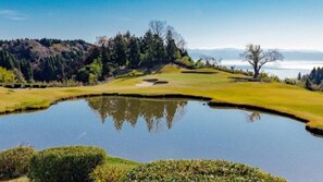 Egy golfpálya, melynek része egy tó, fák és tiszta, kék égbolt.