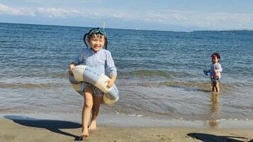 Escena de playa con un niño sosteniendo un juguete y otro niño de pie en el agua.