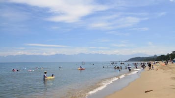 Ein Strand mit badenden und Kajak fahrenden Personen, einem Sandufer und Bergen im Hintergrund.