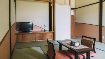 Una habitación japonesa tradicional con suelo de tatami, televisión, una mesita con juego de té y un armario de madera.