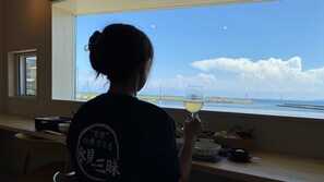 A person seated by a window with a view of the sea, holding a glass of white wine. - Wafu Onsen Motoyu Kano (Himi)