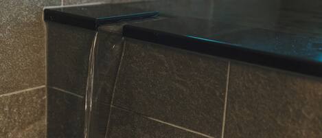 A close-up of a black tiled countertop with a visible water stream.