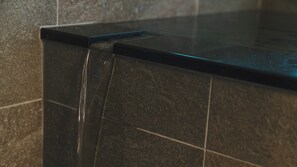 A close-up of a black tiled countertop with a visible water stream. - Wafu Onsen Motoyu Kano (Himi)