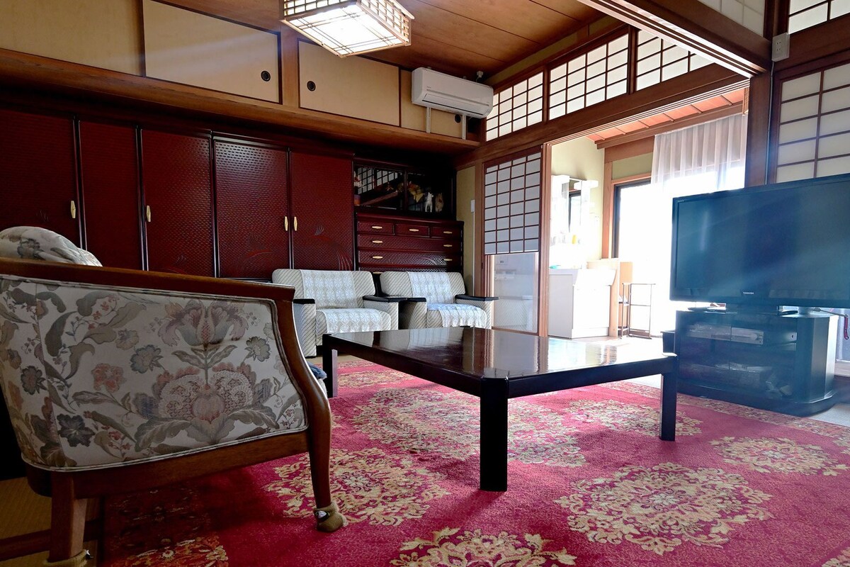 A traditional Japanese-style living room with tatami flooring, a low table, a sofa, and a television.