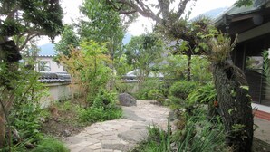 A stone pathway leading through a garden with various plants and trees. - Kashibesso Sakuraso (Beppu)