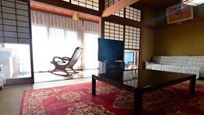 A traditional Japanese room with tatami flooring, a low wooden table, a sofa, and a television. - Kashibesso Sakuraso (Beppu)