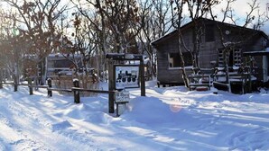 A snow-covered wooden cabin with a signboard in front. - Kuju Aid Station (Kokonoe)