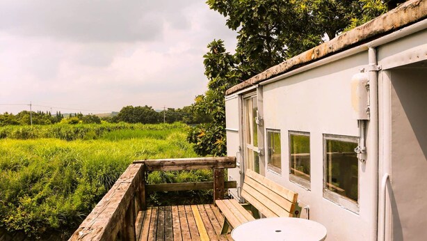 A rustic wooden deck with a bench and table, overlooking a lush green field. - Kuju Aid Station (Kokonoe)