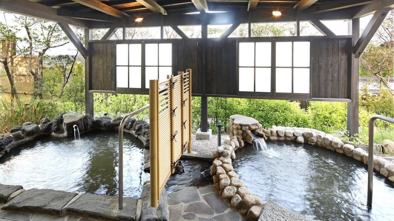 A covered outdoor hot spring area with stone pathways and wooden railings.