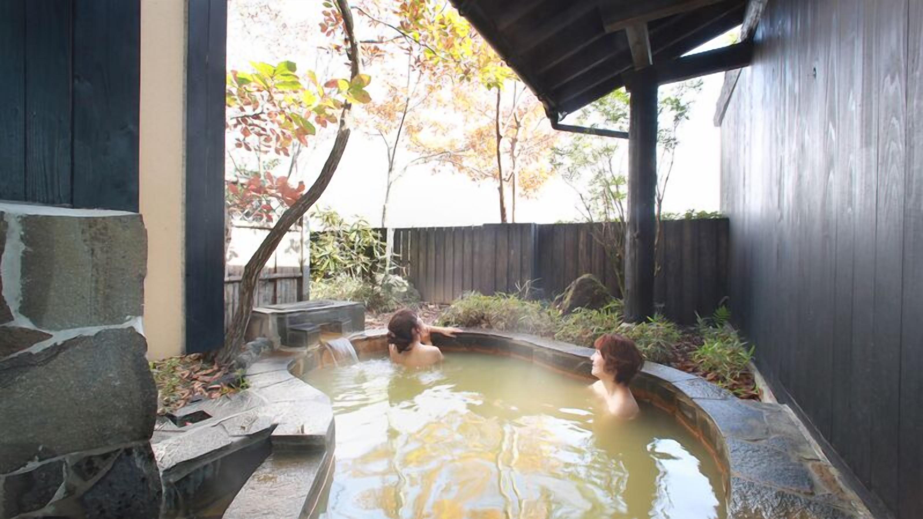A stone hot tub with a wooden deck and a wooden fence in the background.