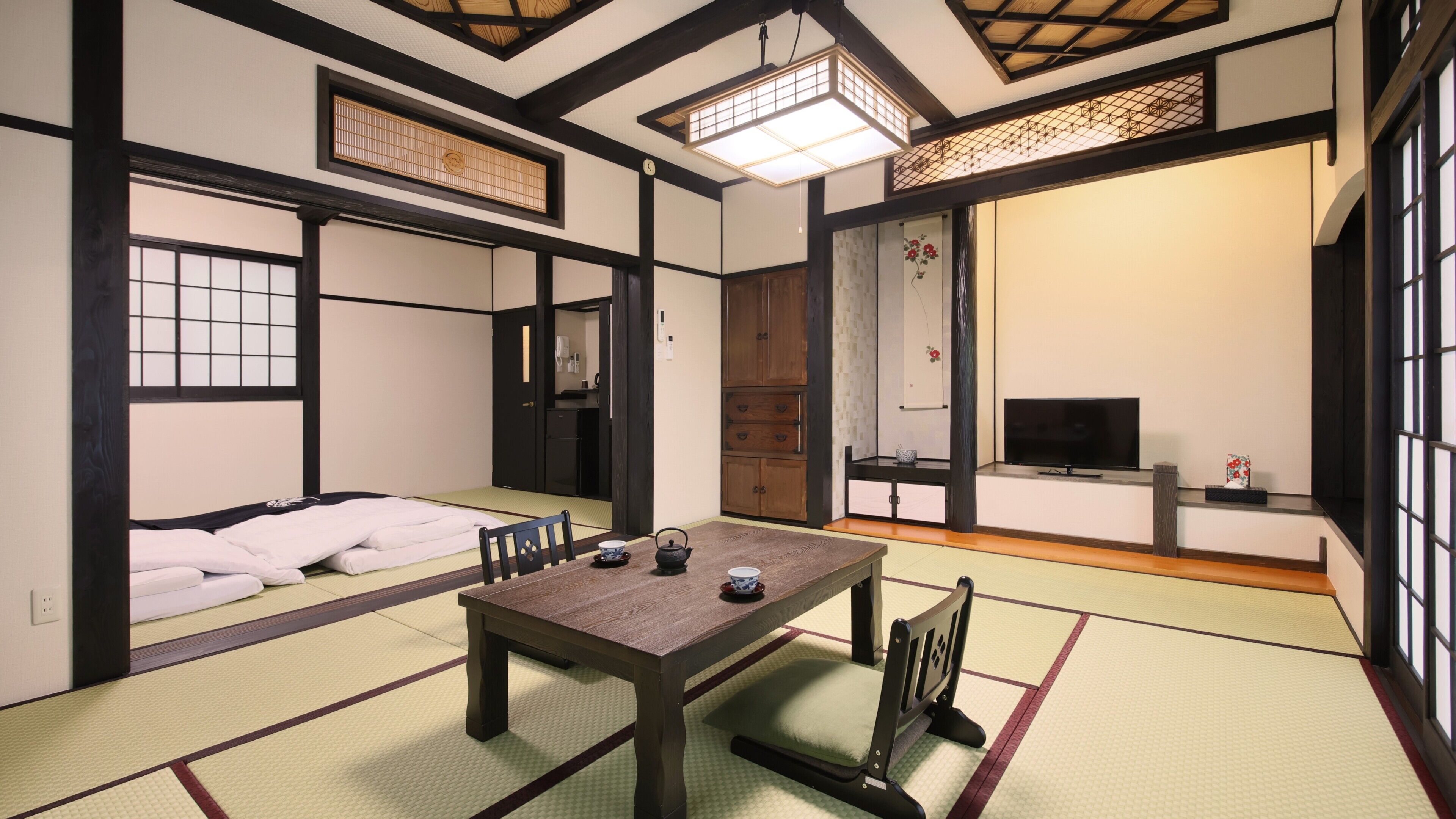 A traditional Japanese room with tatami flooring, a low table with tea set, a television, and sliding doors.