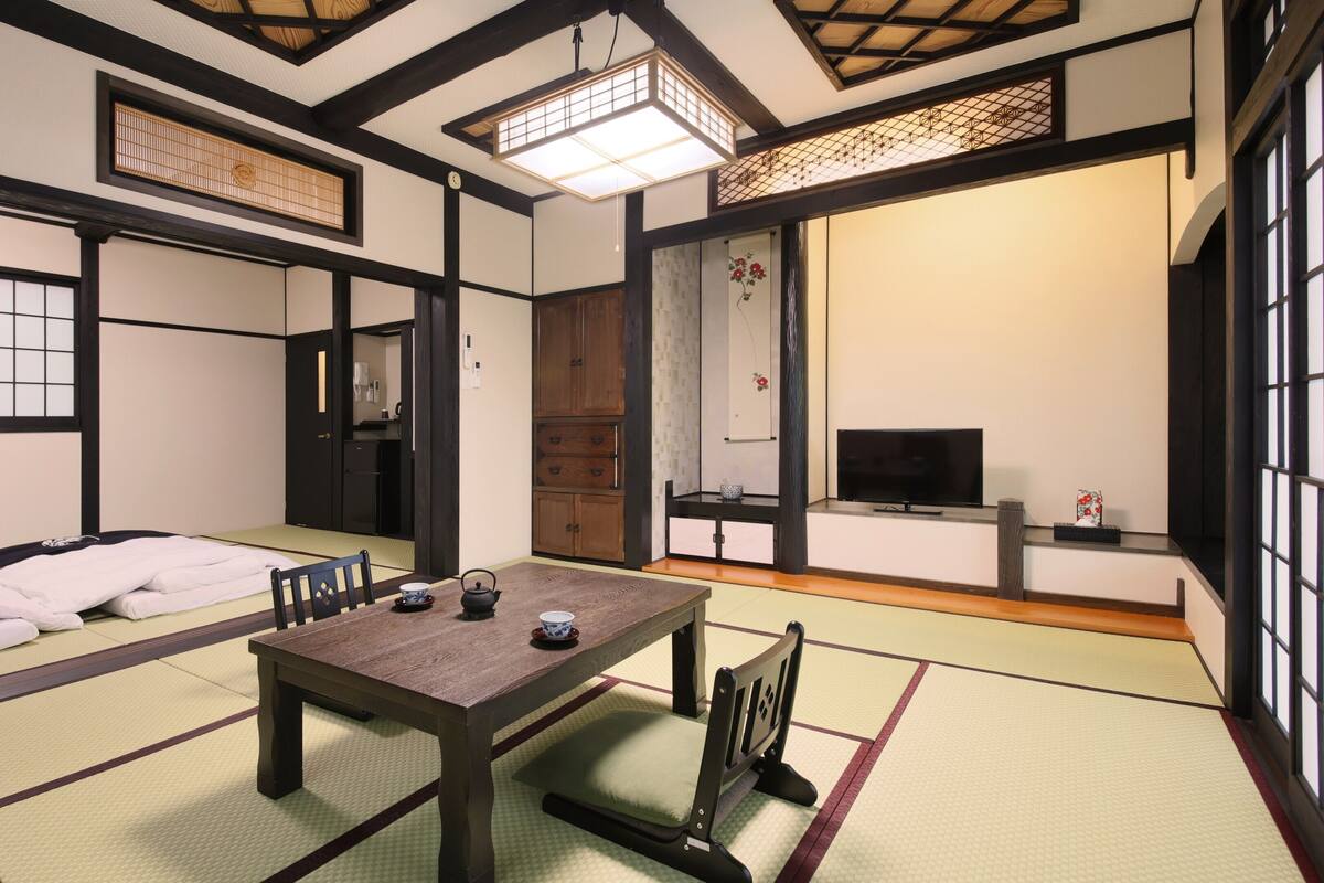 Ein traditioneller japanischer Raum mit Tatami-Bodenbelag, einem niedrigen Tisch mit Teeservice, einem Fernseher und Schiebetüren.