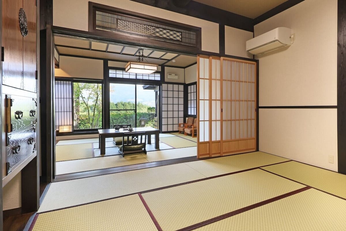 Ein traditioneller japanischer Raum mit Tatami-Böden, Schiebetüren und Blick auf einen Garten.