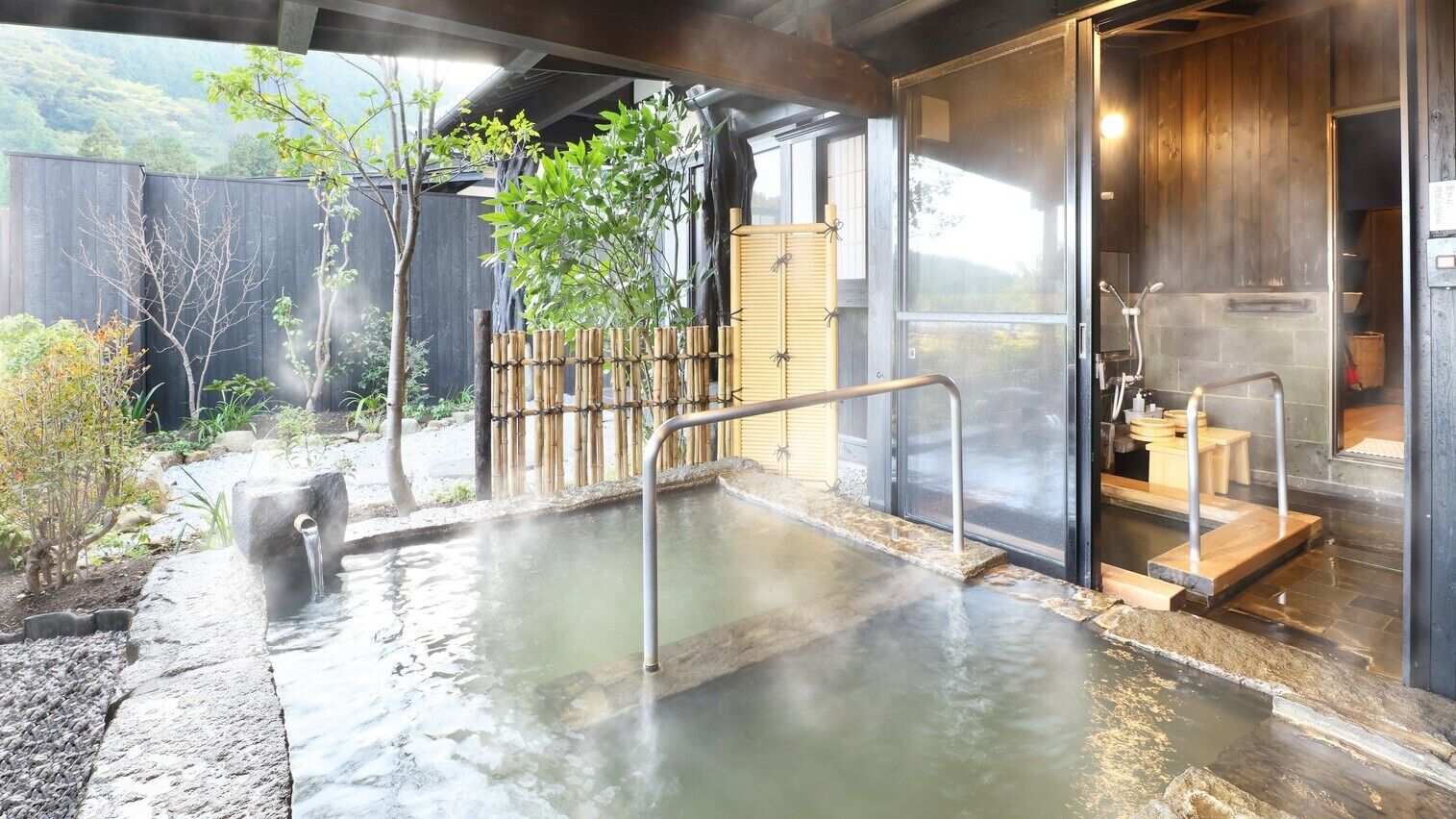 A hot spring bath area with a wooden fence, a stone pathway, and a wooden bench.