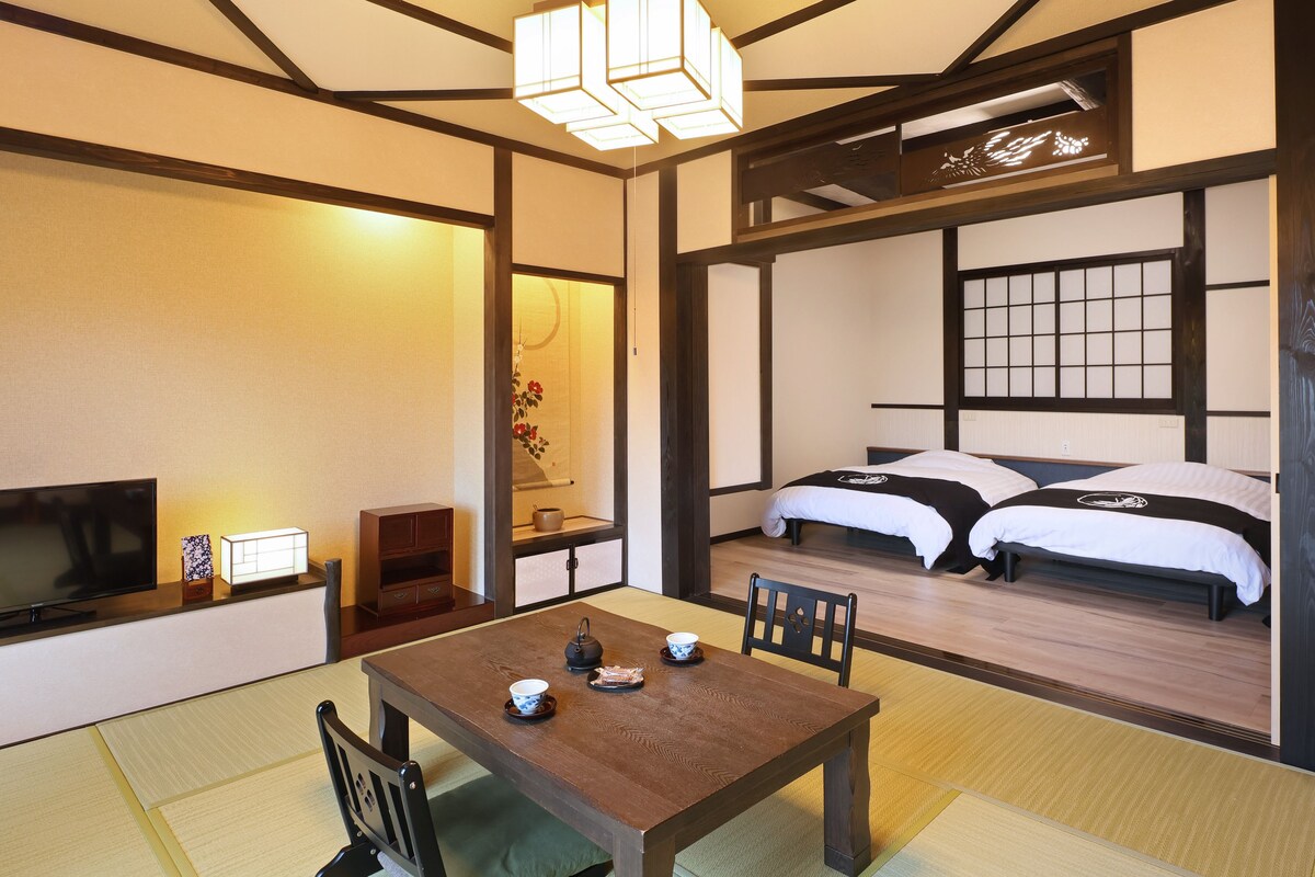 Una habitación japonesa tradicional con suelo de tatami, una mesa baja con un juego de té, un televisor y una cama con futones.