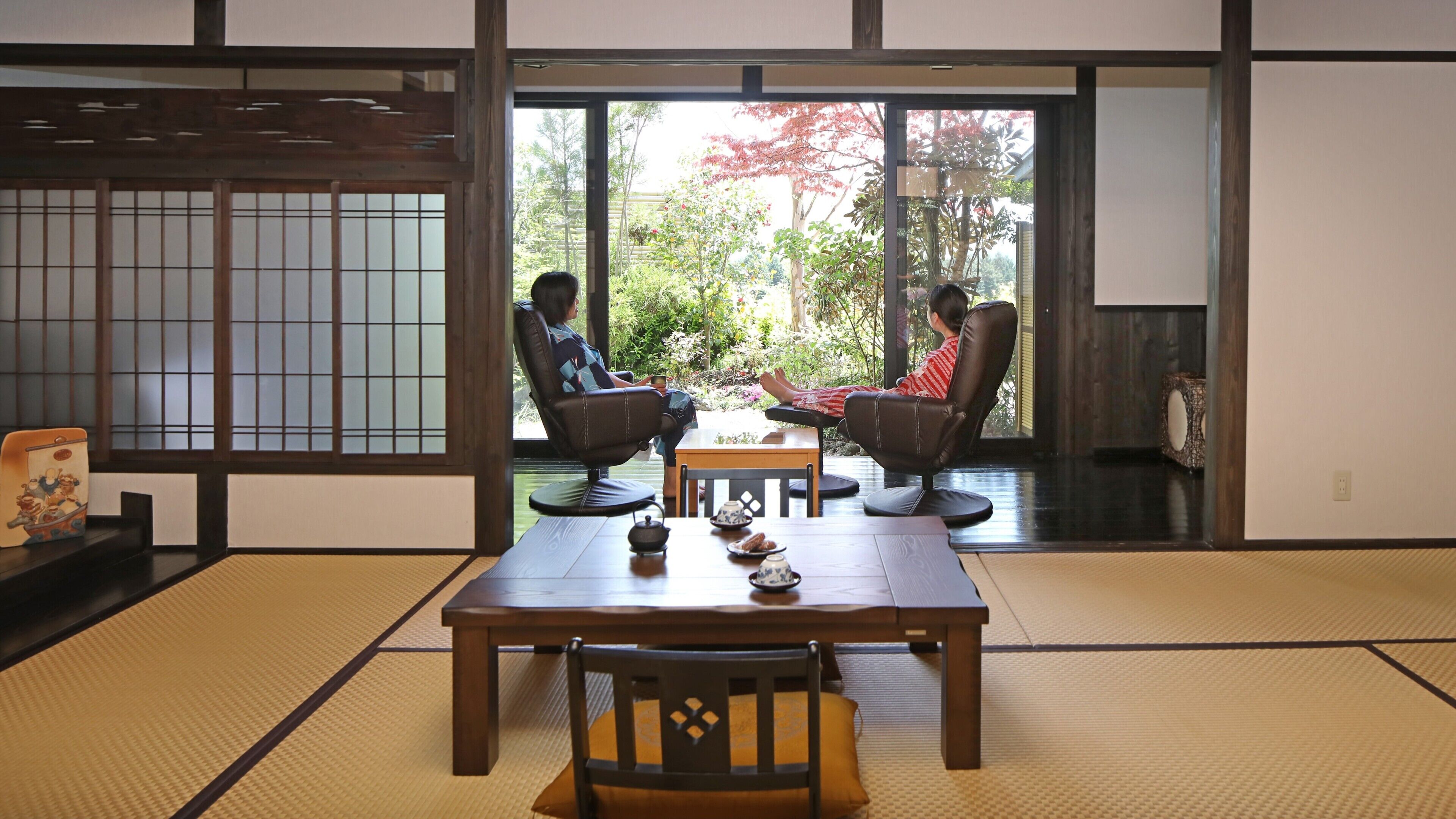 A traditional Japanese room with tatami flooring, a low table, and two chairs.