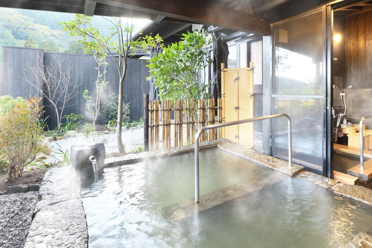 Zona de baños termales con valla de madera, un camino de piedra y un banco de madera.