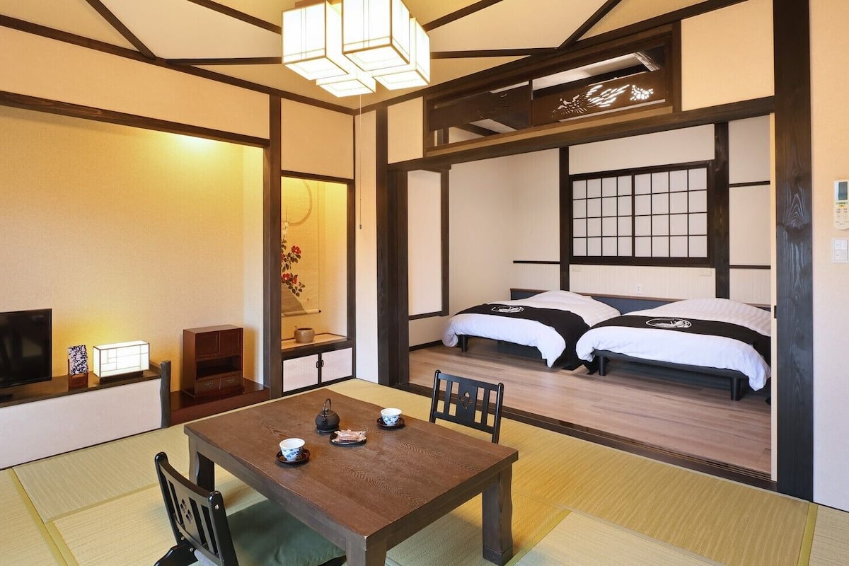 Ein traditioneller japanischer Raum mit Tatami-Böden, einem niedrigen Tisch mit Tee-Service, einem Fernseher und zwei Betten mit schwarz-weiß gestreifter Bettwäsche.