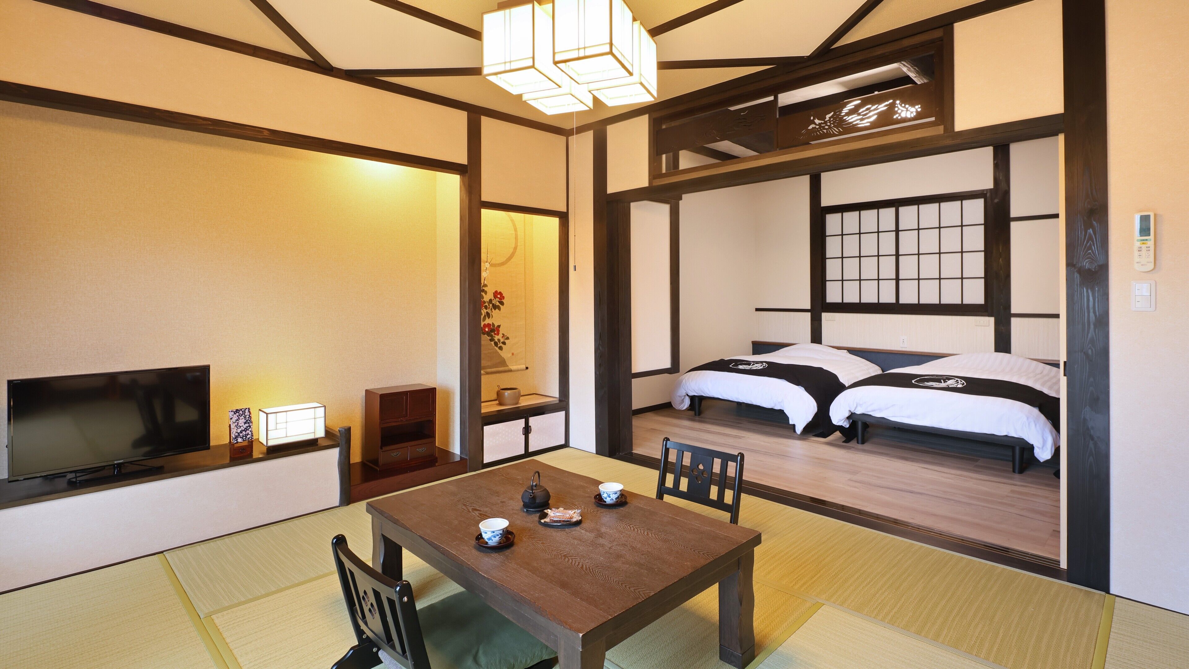 A traditional Japanese room with tatami flooring, a low table with a tea set, a television, and a bed with futons.