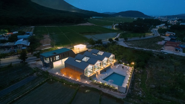 A modern house with a large glass facade, a swimming pool, and a well-lit outdoor area.