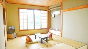 Ein traditioneller japanischer Raum mit Tatami-Bodenbelag, einem niedrigen Tisch, Kissen, einem Fernseher und einer Whiteboard-Tafel.